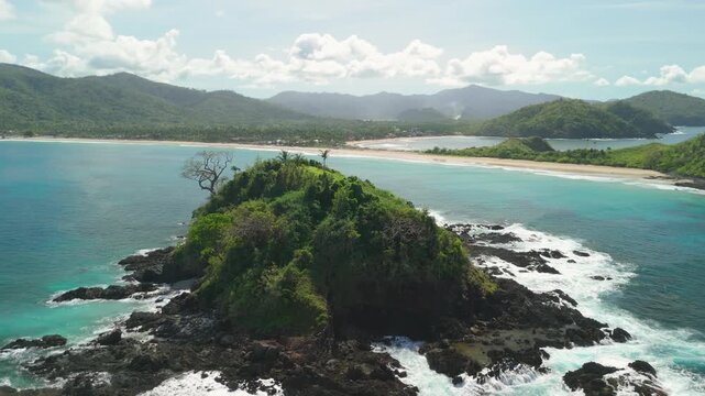 Aerial parallax around small rocky islet with waves and turquoise water and Nacpan Beach in background El Nido Palawan Philippines