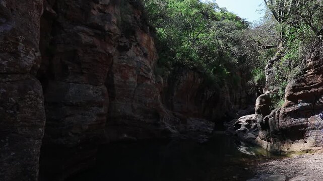 Natural rock pool surrounded by steep canyon walls, layered stone formations, vegetation, and rugged terrain inside La Garita Canyon, Sierra P&eacute;njamo, Guanajuato, Mexico.