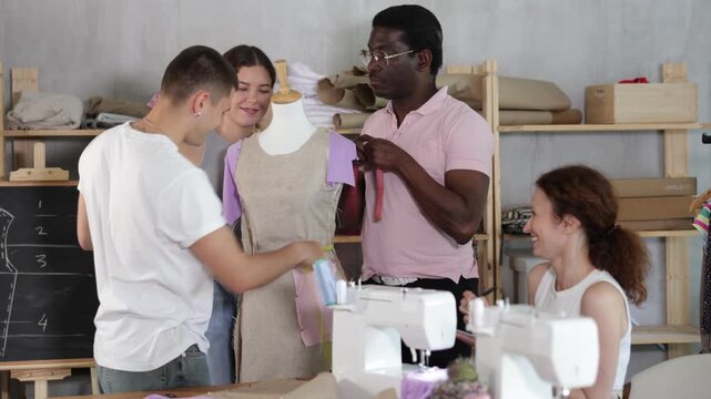 Focused and enthusiastic students of different ages and backgrounds collaborating in fashion design course in sewing workshop, learning garment construction, measurement and dress fitting on mannequin
