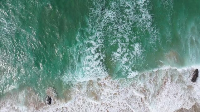 Waves create intricate patterns as they reach the sandy shore, showcasing the vibrant aquamarine hues of the ocean. Suitable for use in travel and nature documentaries.
