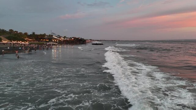 Coastal town at dusk with waves rolling onto dark beach Canggu Bali aerial drone video