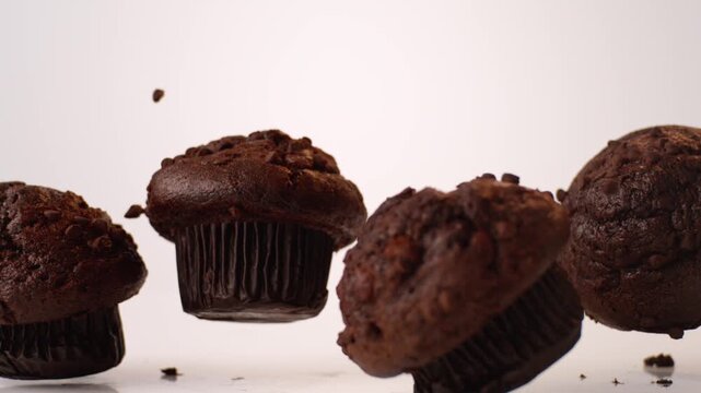 Chocolate-studded muffins bouncing and tumbling on white in slow motion macro studio shot. kids lunchbox content, school breakfast ads, after school snack reels.