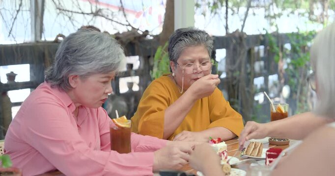 Senior Asian women eat cake together at cafe table during reunion brunch, sharing dessert, iced drink, quiet conversation, companionship, comfort, friendship renewal, relaxed later life connection.