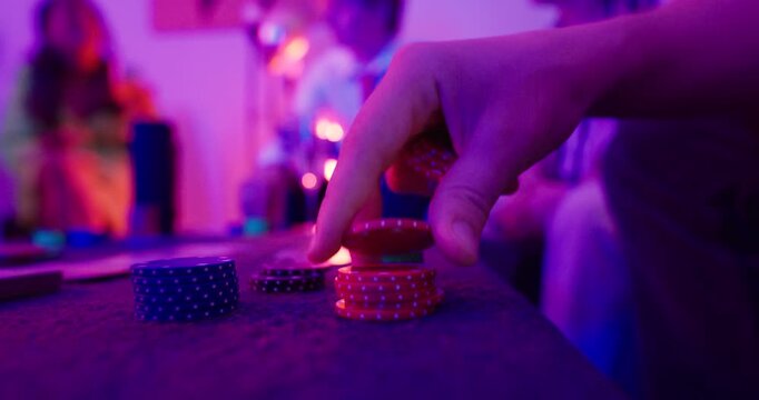 Close-up stock video showing a hand stacking poker chips in colorful neon lighting. Suitable for gambling, casino games, betting, poker nights, risk taking, entertainment, and gaming concepts.