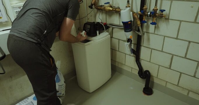 checking and maintaining a water softener system in a basement utility room. Suitable for water treatment, descaling maintenance, household technology, plumbing inspection, and home service concepts.