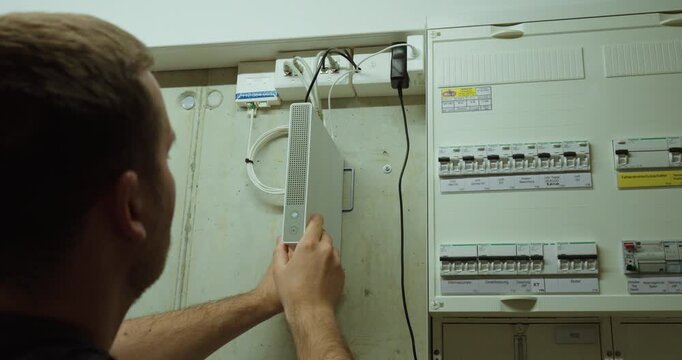 man inspecting a WiFi router inside a utility room near an electrical panel. Suitable for internet troubleshooting, home network setup, router maintenance, connectivity problems, and technology