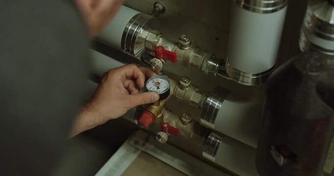 Person inspecting a pressure gauge and adjusting a valve on a heating or plumbing system to monitor and release system pressure.