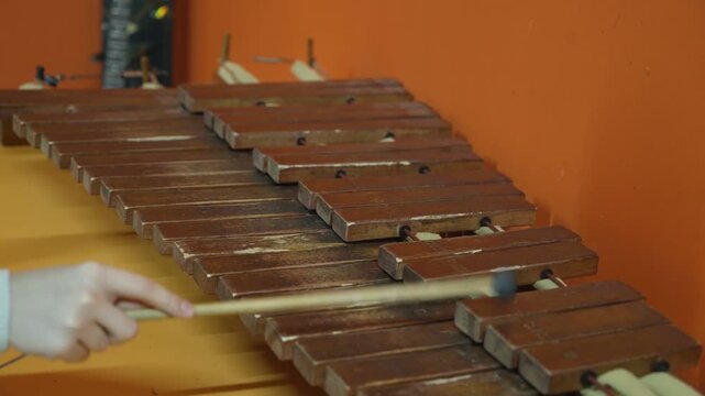 Person playing wooden xylophone with mallets against orange wall background close up view.