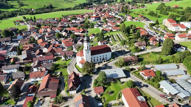 Orbit flight around parish church St. Ulrich in village Wertach with houses and meadows in Allg&auml;u Alps, Bavaria, Germany