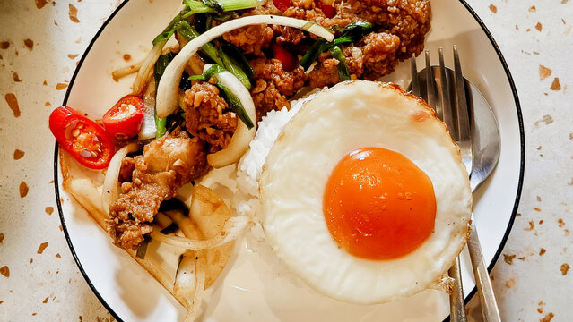 Delicious Thai Basil Chicken Stir Fry with Sunny Side Up Egg Served on a Plate with Jasmine Rice for a Traditional Asian Lunch Meal