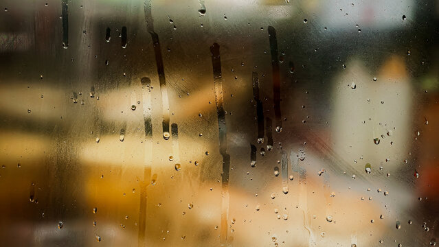 Raindrops on a window pane with soft bokeh background light for a moody rainy day texture and tranquil indoor atmosphere
