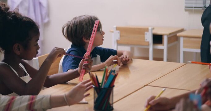 Elementary school children having fun looking through colorful transparent rulers during a lesson.