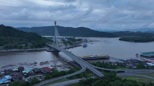 Aerial drone descending and tilting left toward Raja Isteri Pengiran Anak Saleha cable-stayed bridge over Brunei River, Bandar Seri Begawan, Brunei at dusk