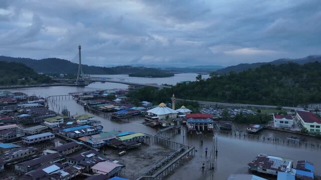 Aerial drone rising with left tilt from Kampong Ayer water village toward Raja Isteri Pengiran Anak Saleha cable-stayed bridge, Bandar Seri Begawan, Brunei at dusk