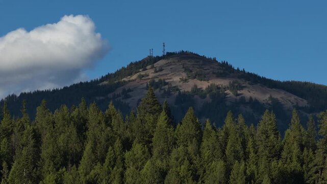 Aerial of Wardner Peak in Kellog Idaho in Shoshone County in spring featuring dense evergreen trees and rolling terrain under a blue sky with scattered clouds