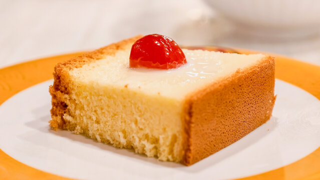 A delightful slice of plain cake with a cherry on top, served on a white plate with an orange rim