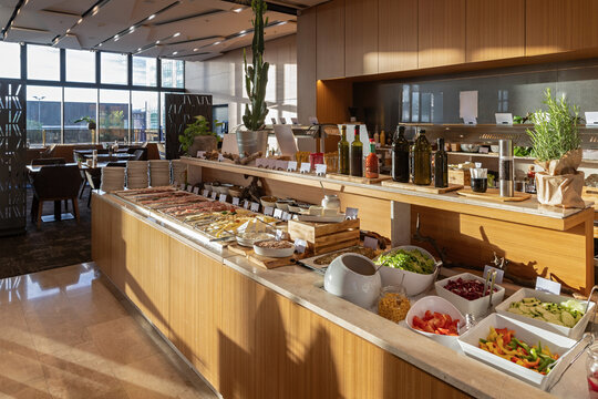 Modern hotel buffet station with fresh salad bar and cold cut platters in morning sunlight