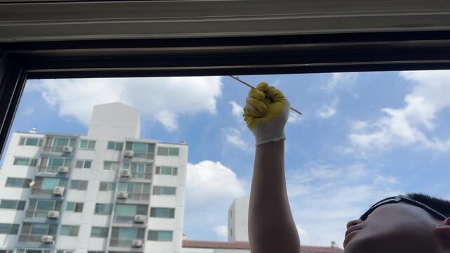 Skilled construction worker uses a wooden spatula tool to smooth and shape freshly applied silicone sealant along a window frame joint on a high-rise residential building. 