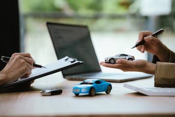 Fototapeta premium Close-up of a car sales or leasing consultation, with a miniature vehicle presented to a customer, symbolizing auto financing, ownership transfer, vehicle purchase, and rental services.