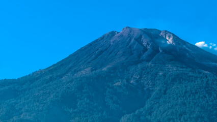 Fototapeta premium Majestic Volcano Peak Rising into a Clear Blue Sky with Forested Slopes Below
