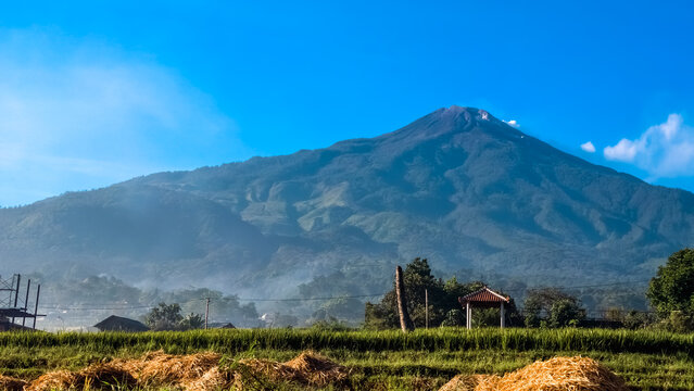 Majestic Mountain Peak Rising Above Lush Green Rural Fields Under a Clear Blue Sky