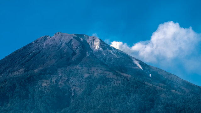 Majestic volcanic peak under a brilliant blue sky, gently emitting a wispy plume of smoke, showcasing the awe-inspiring power and serene beauty of Earth's natural geological formations