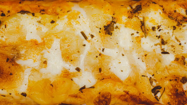 Close up of golden brown cheesy scalloped potatoes with aromatic herbs in a baking dish
