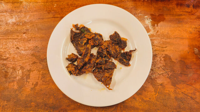 A mouth-watering view of a plate of delicious crispy fried lungs, rich in flavor and texture, served on a clean white plate against a warm rustic wooden backdrop, ready to be enjoyed.