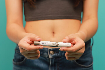 Weight loss transformation concept shown by woman holding GLP 1 injection pen in front of bare...