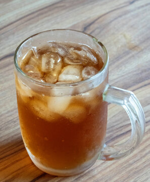 Refreshing glass of cold iced tea with ice cubes on a wooden table