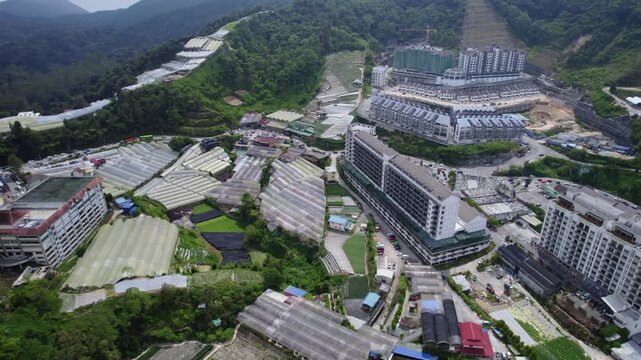 Drone reveal showcasing the unique landscape of Cameron Highlands, Malaysia, where greenhouse agriculture, high-rise developments, roadways, and mountain terrain coexist within a thriving community.