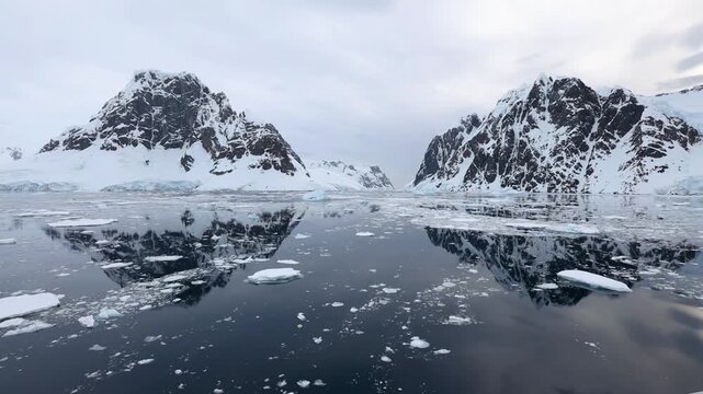 Lemaire Channel in Antarctica featuring snow-covered mountains towering over calm, icy waters. Massive icebergs drift through the glacial terrain, highlighting the untouched wilderness of the Southern