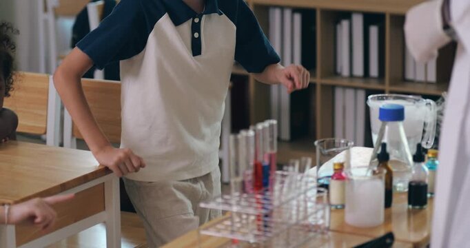 A young boy with glasses listens carefully as a teacher explains a science experiment with colorful test tubes.