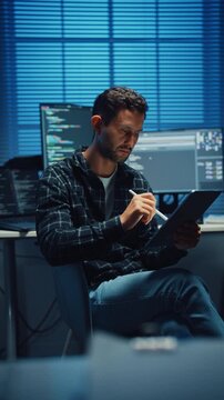 Vertical Screen : Young Caucasian male programmer use tablet for code design and plan in office at night. AI technology, cybersecurity, software developer, freelance innovation, digital data network.