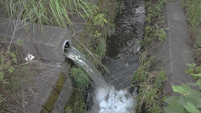 Industrial wastewater rushing out of a concrete pipe into a drainage ditch or canal
