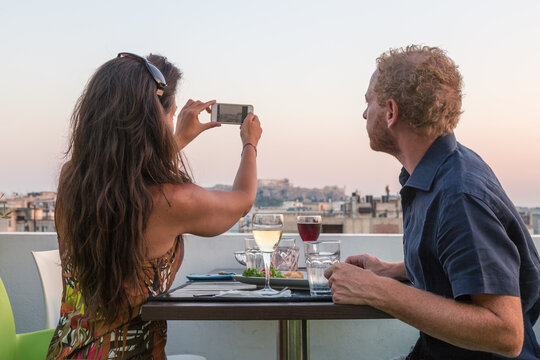 Couple taking a smartphone photo of the Acropolis at sunset, Athens, Greece