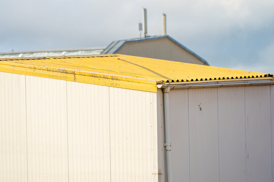 An exterior view of an industrial warehouse container facility with white sandwich panels and a weathered yellow metal roof structure