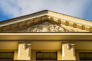 Classical architectural elements showcasing intricate stucco bas-relief sculptures and stone carvings on a yellow residential house gable © K