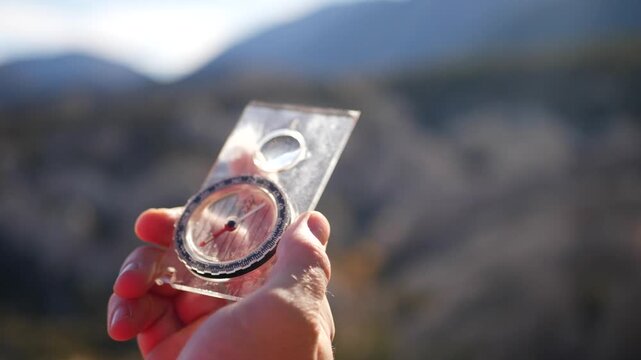 Person holding navigational compass while trekking in mountains during golden hour.