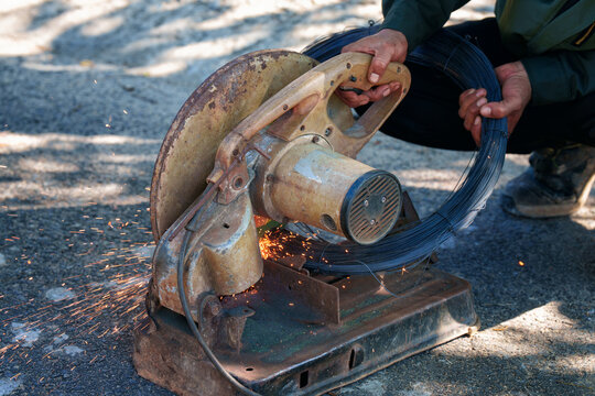 Worker hands cutting roll of steel wire with an electric chop saw machine, bright sparks flying. Industrial work concept.