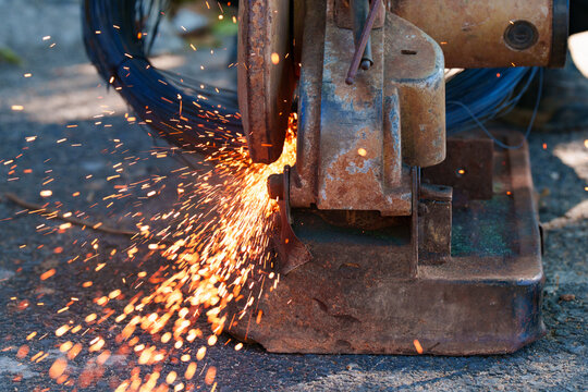 Close up of metal cutting machine with bright orange sparks flying out during industrial work. Construction concept.