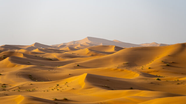 Sunlight shines on the sand dunes of Erg Chebbi near Merzouga. The landscape shows rolling dunes with various shapes and shadows, creating a unique scene in the Sahara Desert.