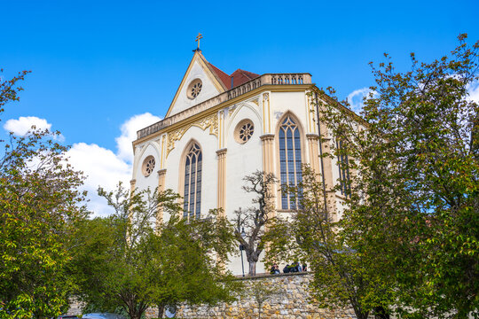 Visitors admire the Church of St. James the Elder in Boskovice, Czechia. Trees surround the church as people explore the area on a sunny day in spring.