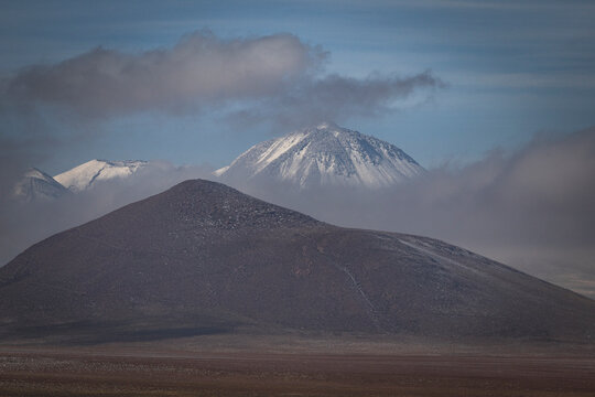 Distant snow capped volcanoes behind barren hills