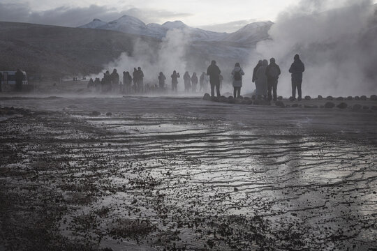Silhouetted crowd watching geothermal geysers at dawn