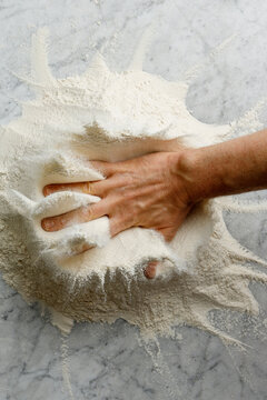 The pizza maker's hand falls on the flour and it scatters