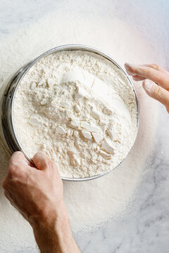 A pizza maker sifts durum wheat flour through a sieve