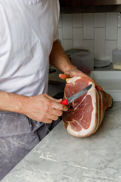Pizzaiola in a pizzaria demonstrates quality jamon before slicing