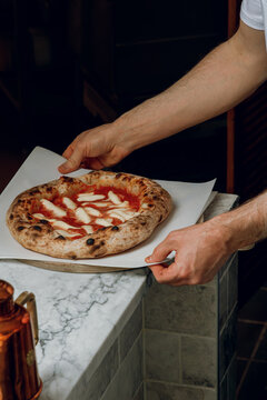 A pizza chef takes a freshly made hot pizza out of the oven