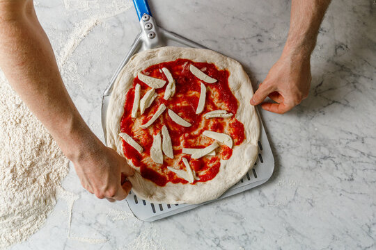 Pizza maker placing pizza on a spatula for baking in the oven